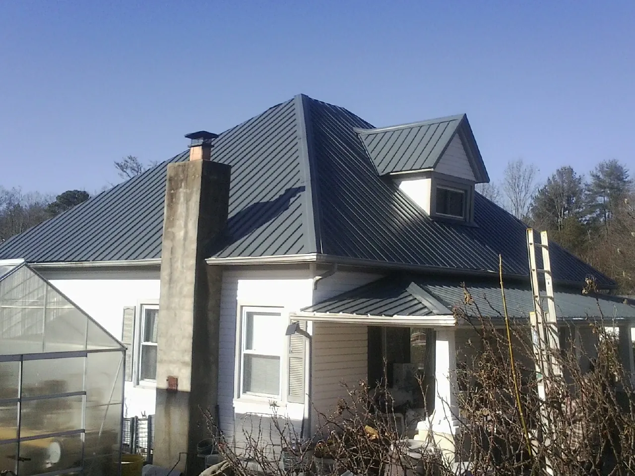 Dark blue standing seam metal roof on a white farmhouse with dormer — Slate & Tile Roof Repair by Roofing Brothers in Lake Mills
