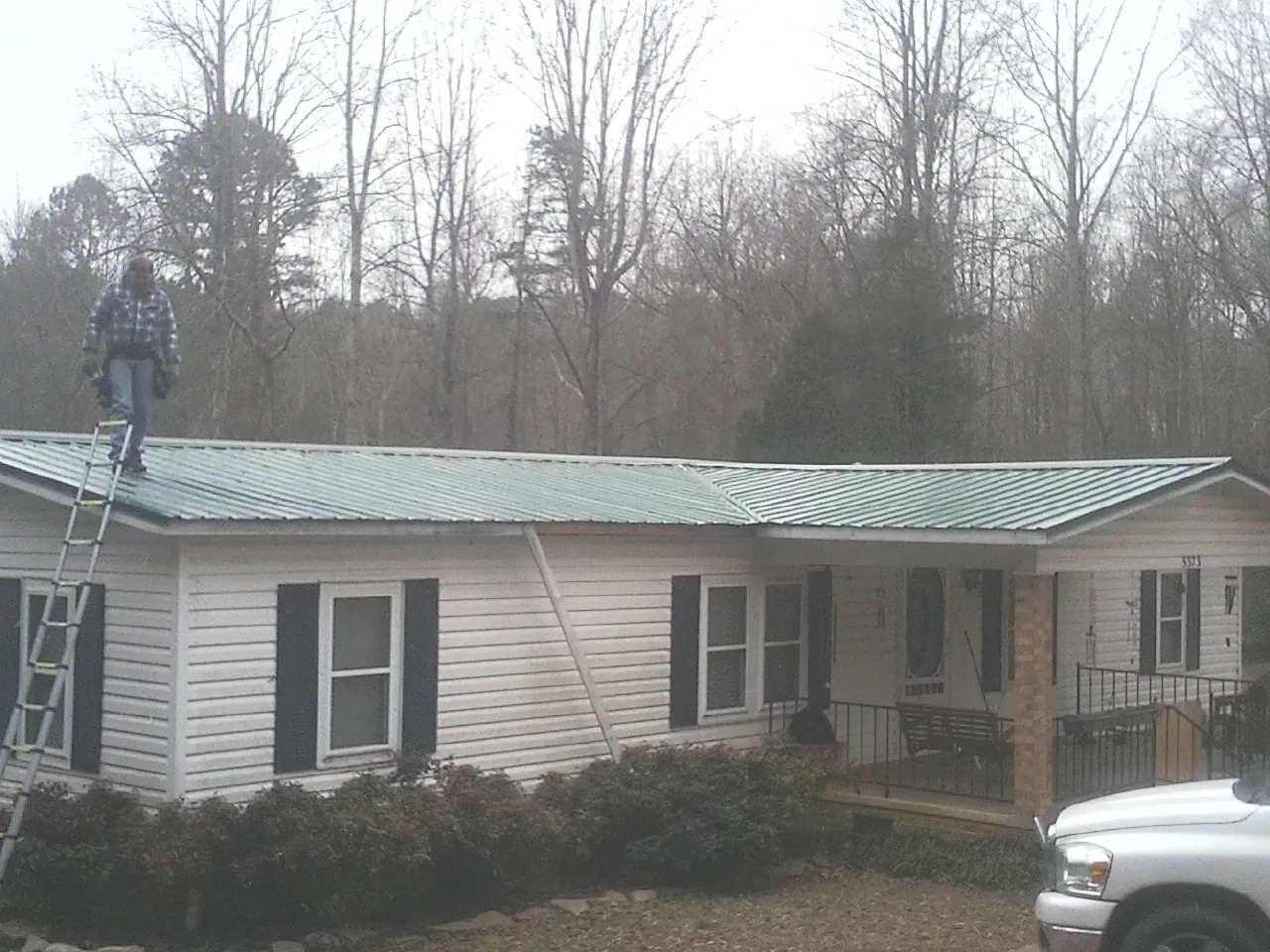 Worker on a ladder beside a new green metal roof on a ranch home in Lake Mills