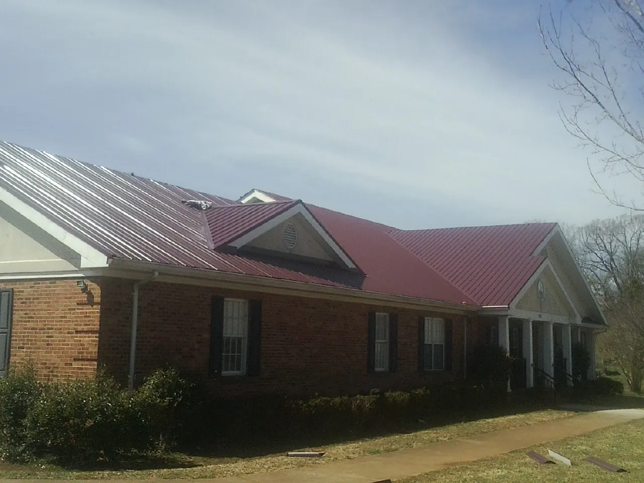 Red metal roof with gabled entries on a long brick building, from a Hail Damage Roof Repair job in Lake Mills