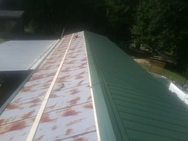 Old rusted panels beside newly installed green metal roofing — Wind Damage Roof Repair by Roofing Brothers in Lake Mills