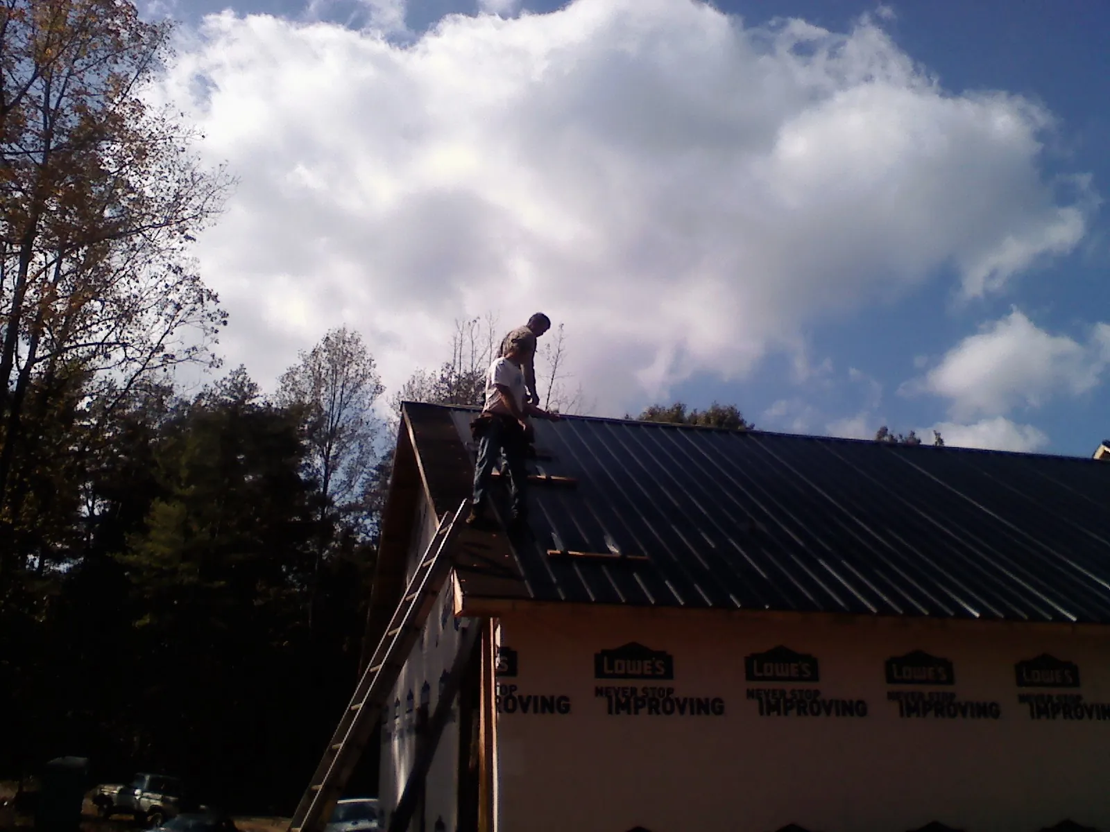 Roofer fastening dark metal panels high against a cloudy sky, from a Roof Inspection job in Lake Mills