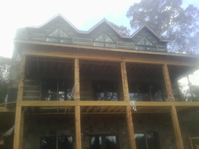 Dormers and porch framing on a large log home under construction — Roof Coating work by our crew in Lake Mills